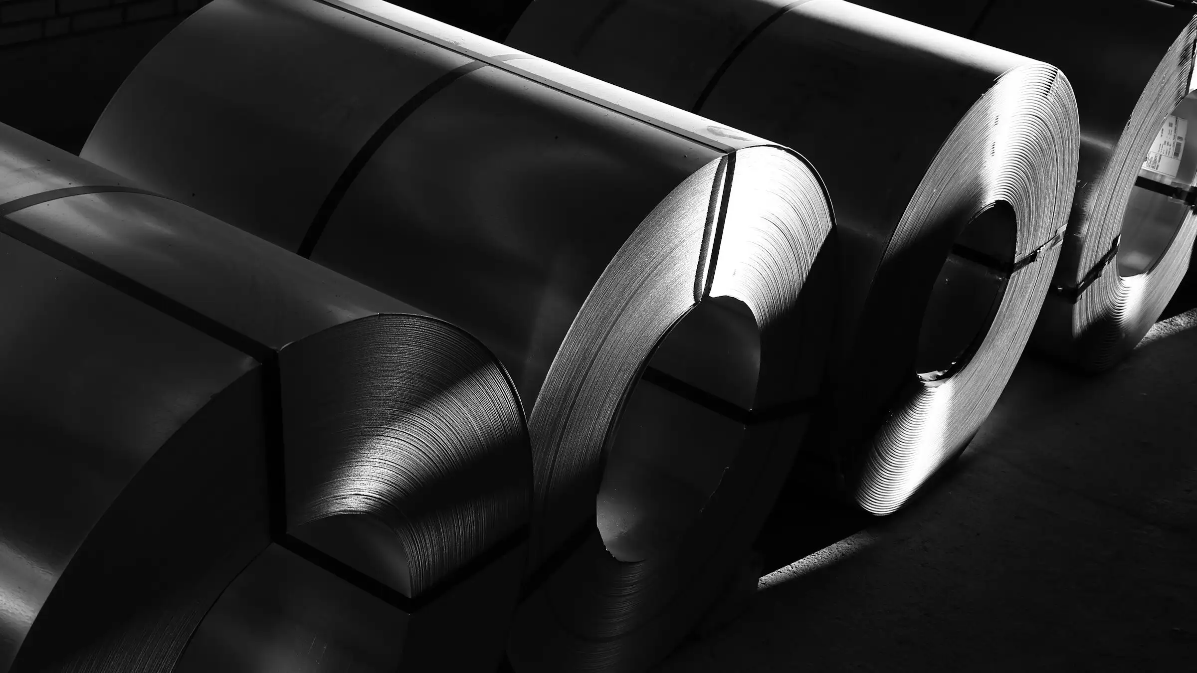 Banded steel coils lying in a row, photographed in black and white.