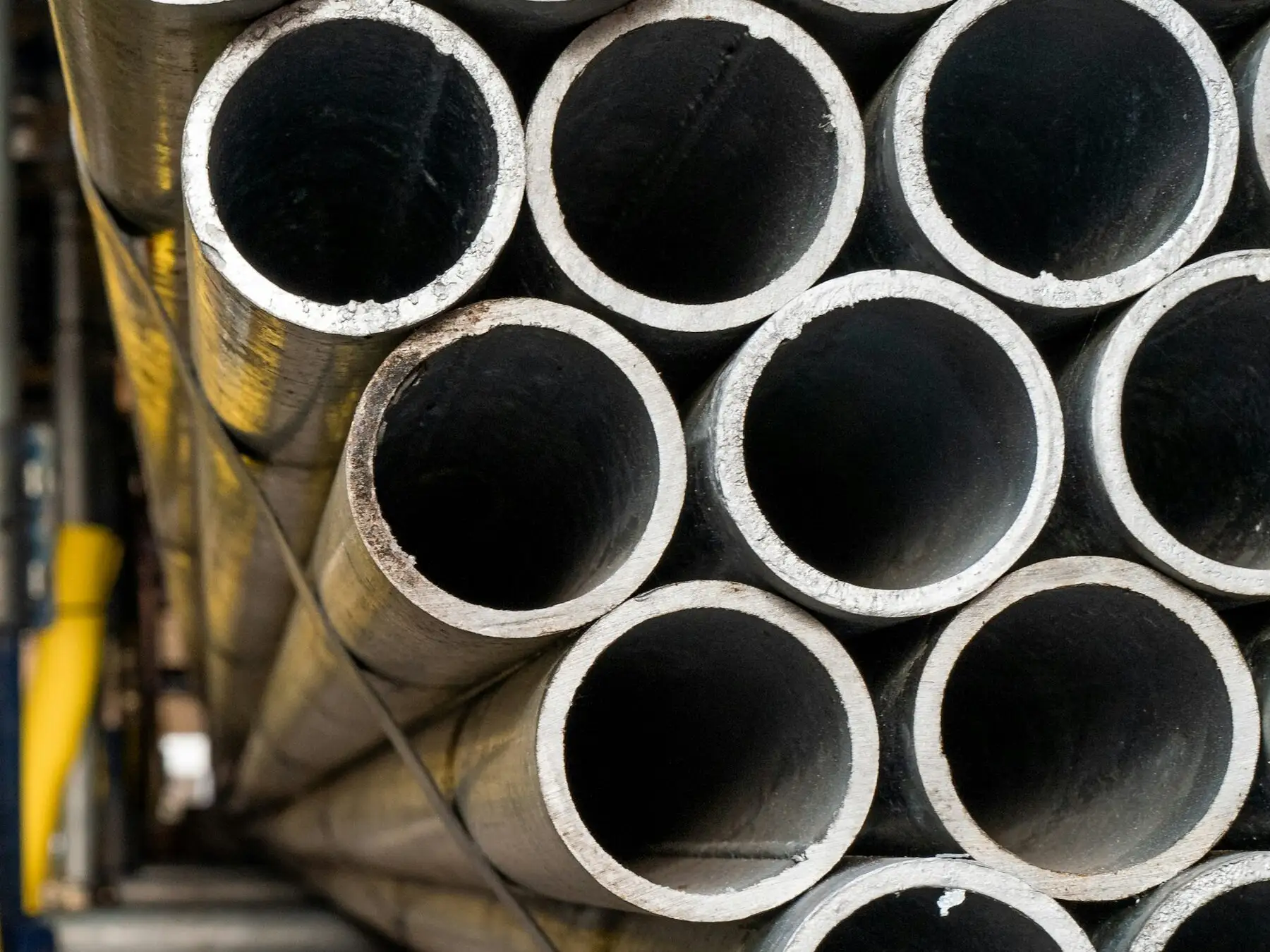 A strapped bundle of galvanized steel pipes seen end-on, showing the zinc-coated surface and the wall of each pipe.