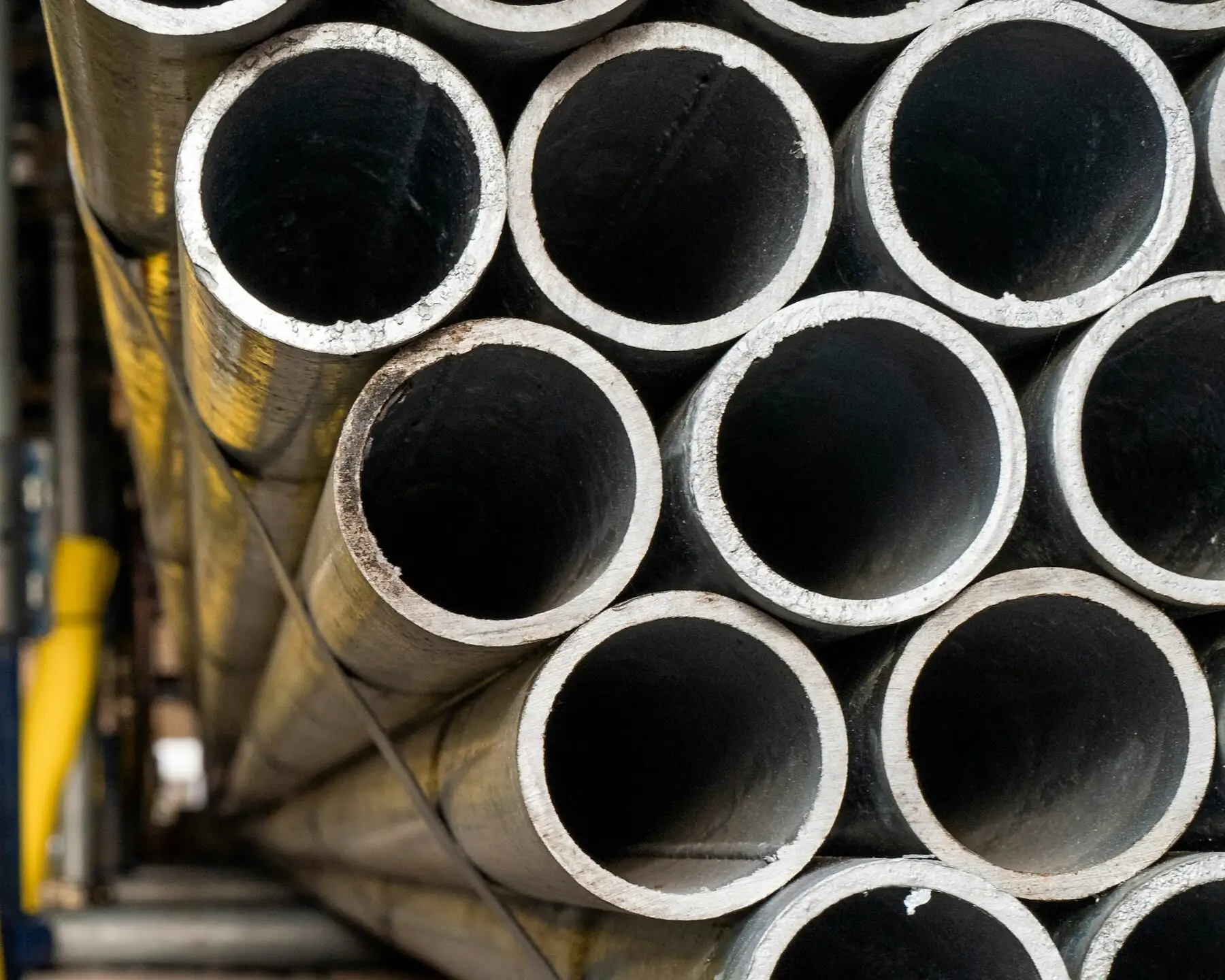 A strapped bundle of galvanized steel pipes seen end-on, showing the zinc-coated surface and the wall of each pipe.