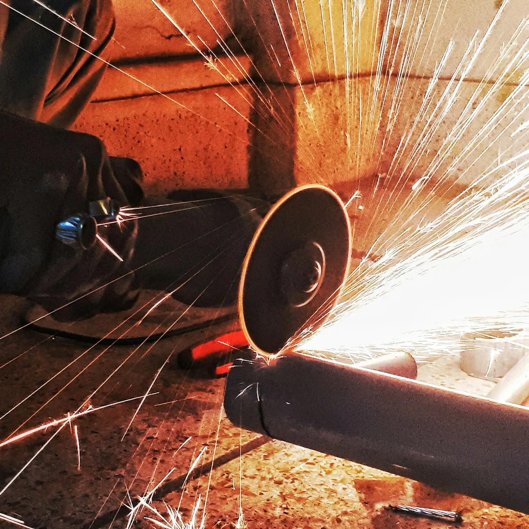 An abrasive disc cutting through a steel pipe, throwing a fan of sparks.