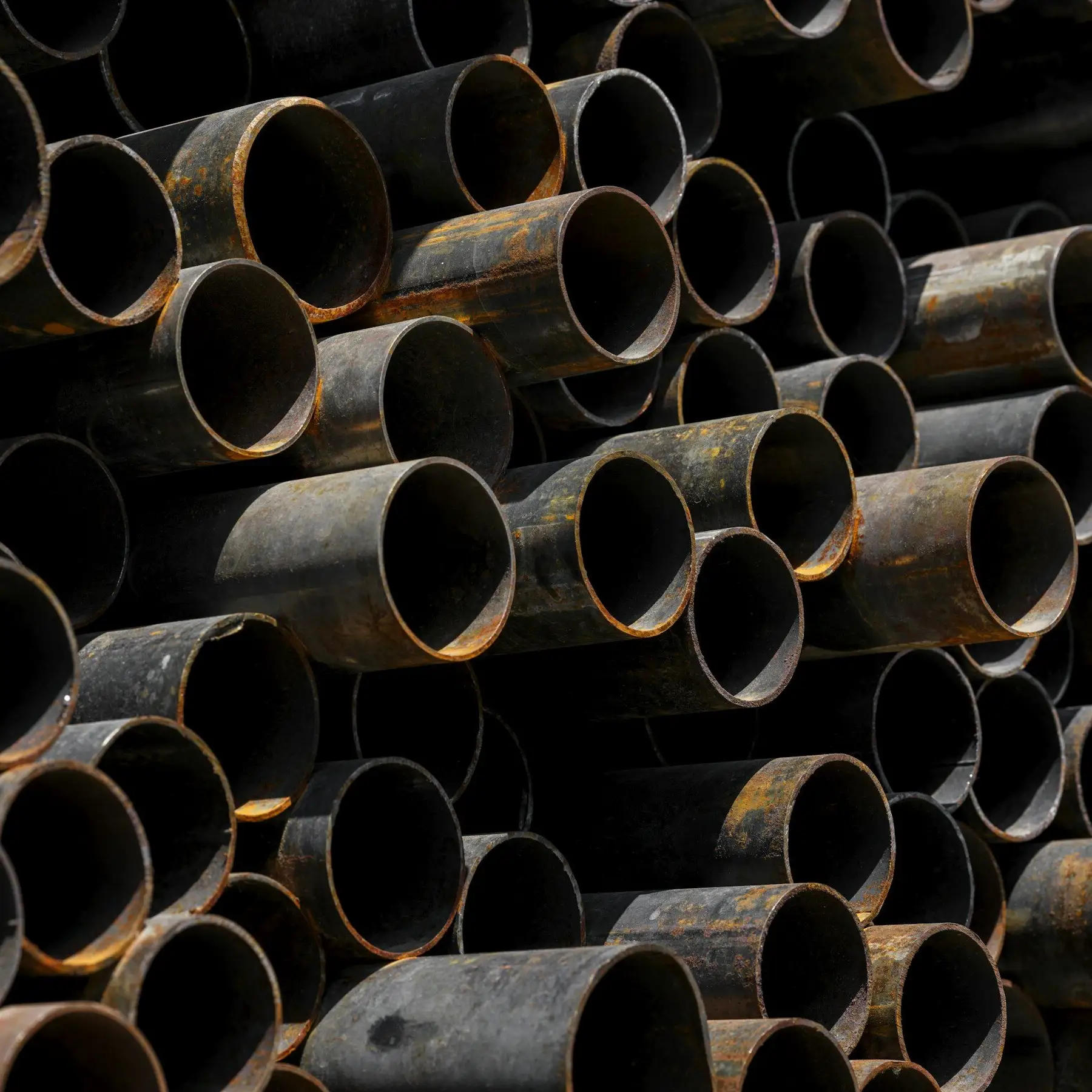A stack of black steel pipes seen end-on, with light rust on the cut ends.