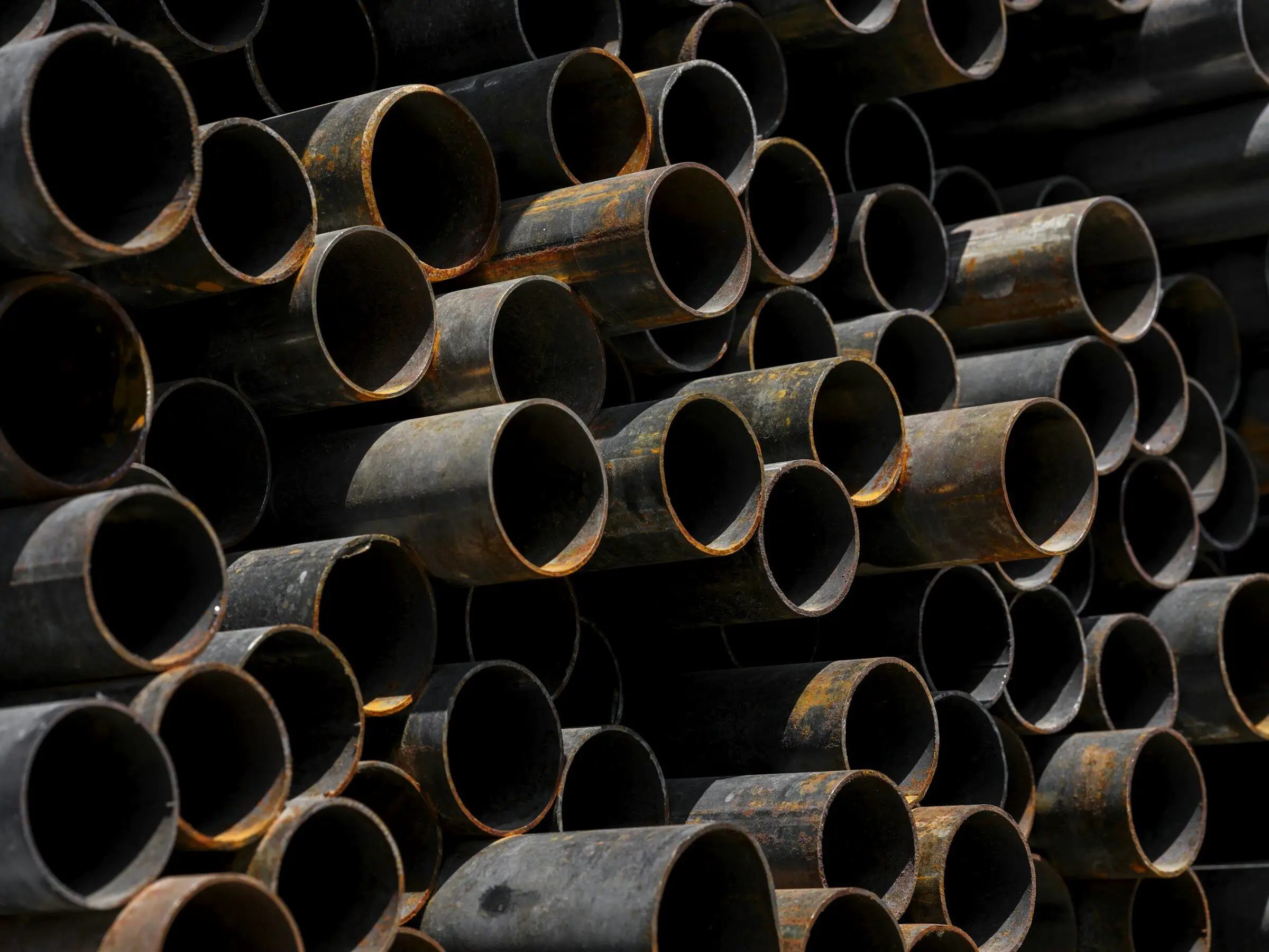 A stack of black steel pipes seen end-on, with light rust on the cut ends.