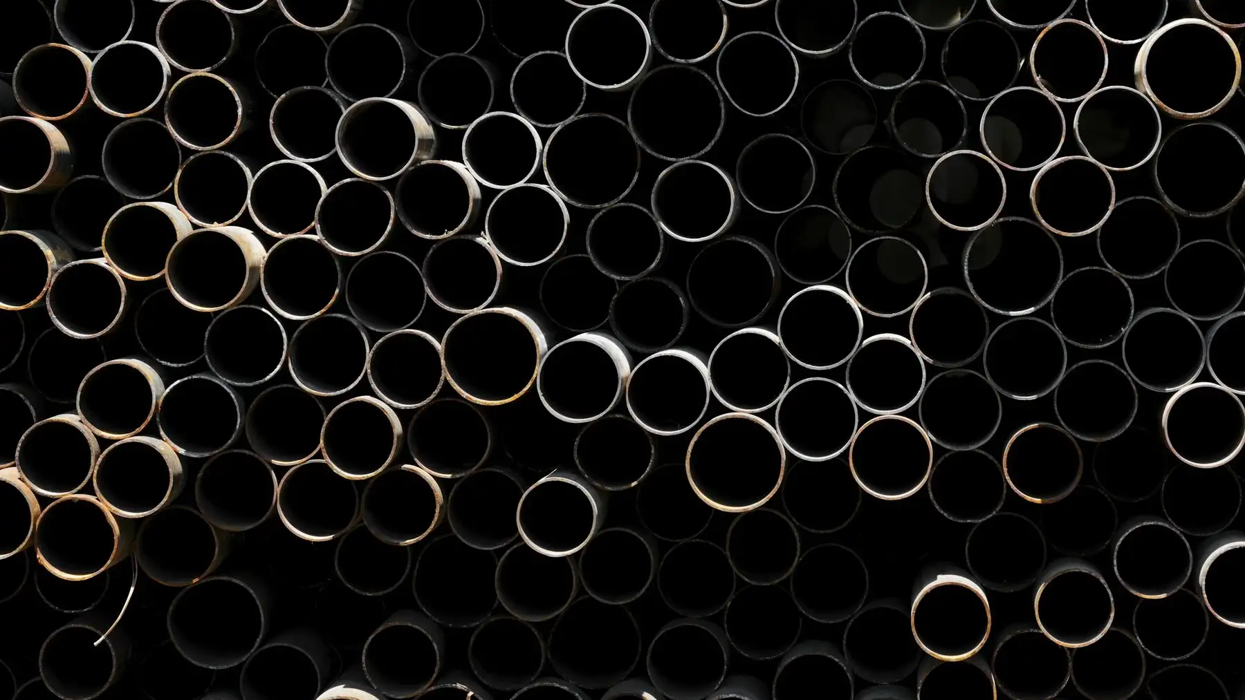 Hundreds of pipe ends packed together in a stack, seen straight on against darkness.