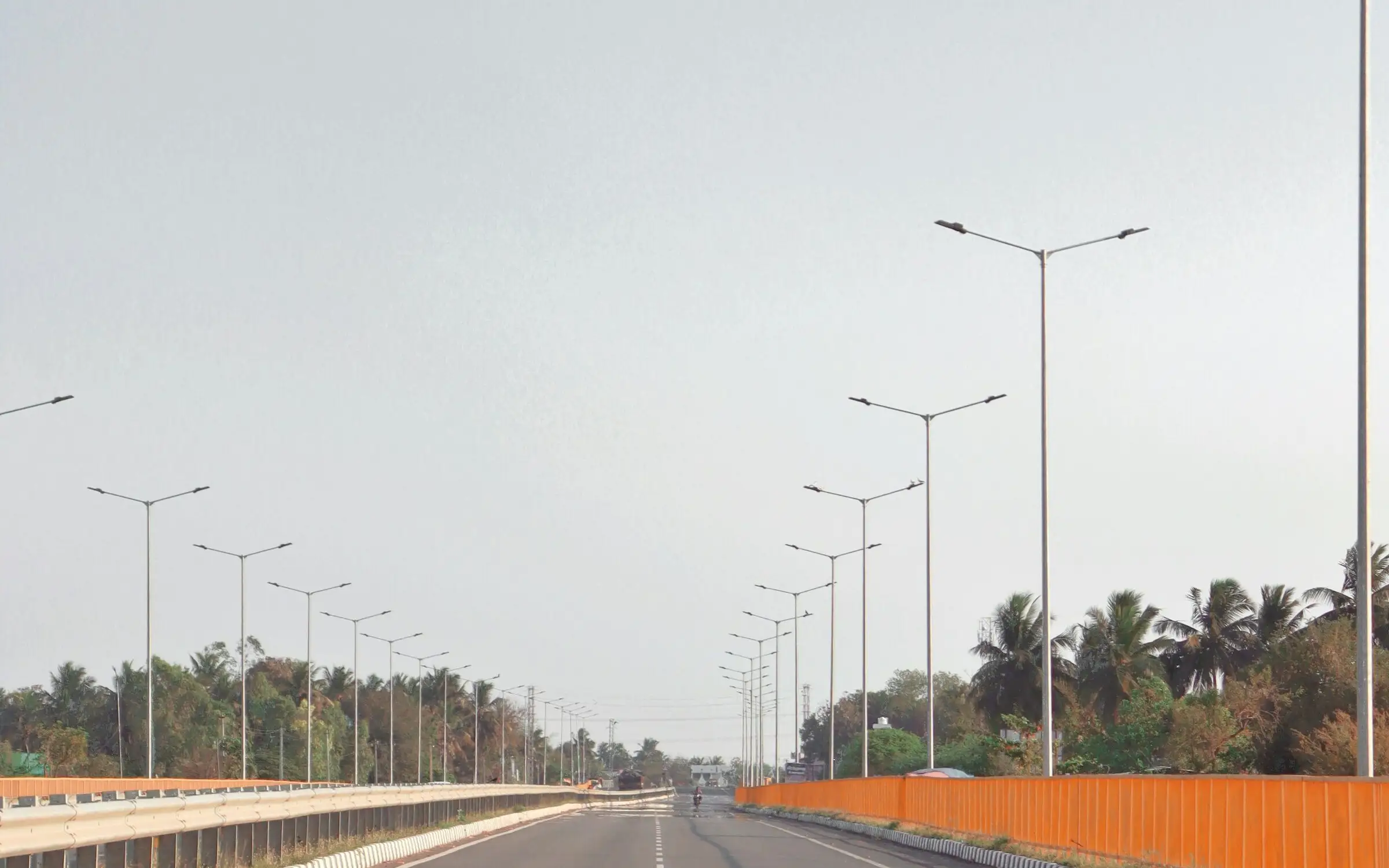 Rows of steel street light poles with twin arms lining both sides of an empty highway.