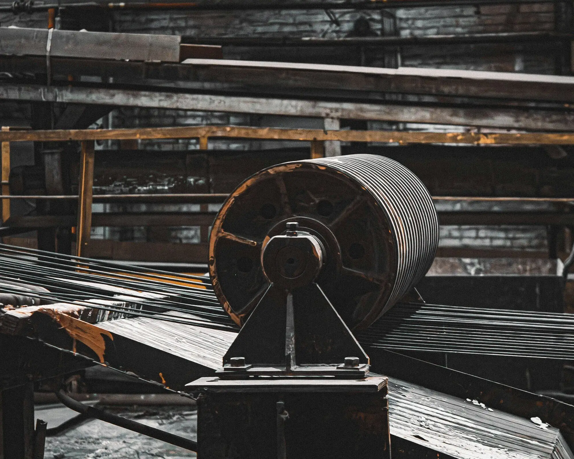 Steel strip and bar running over a roller table beside a large drum in a mill.