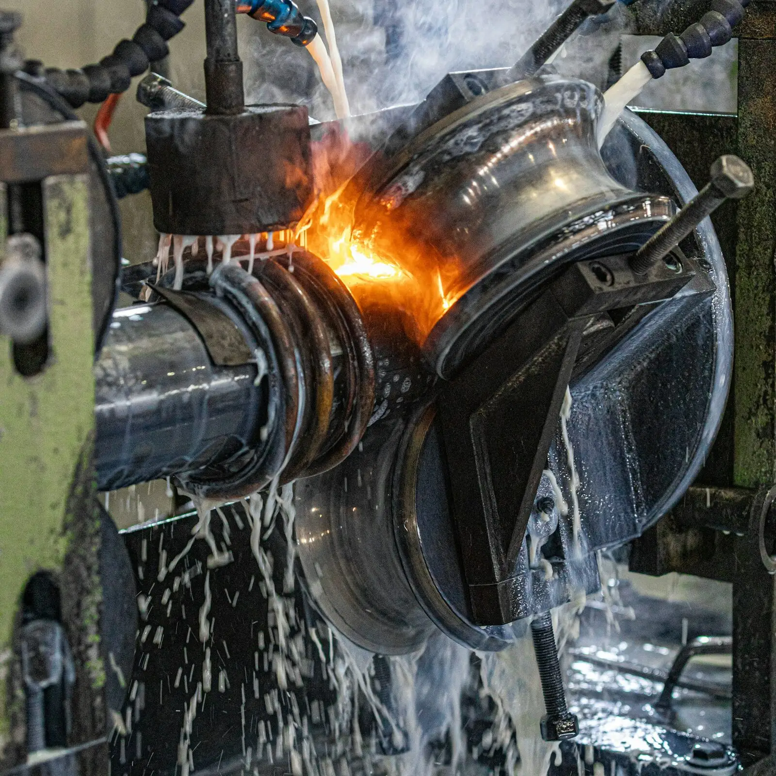 Close-up of a tube mill weld station: the strip glows orange at the seam between steel squeeze rolls while coolant pours over them.