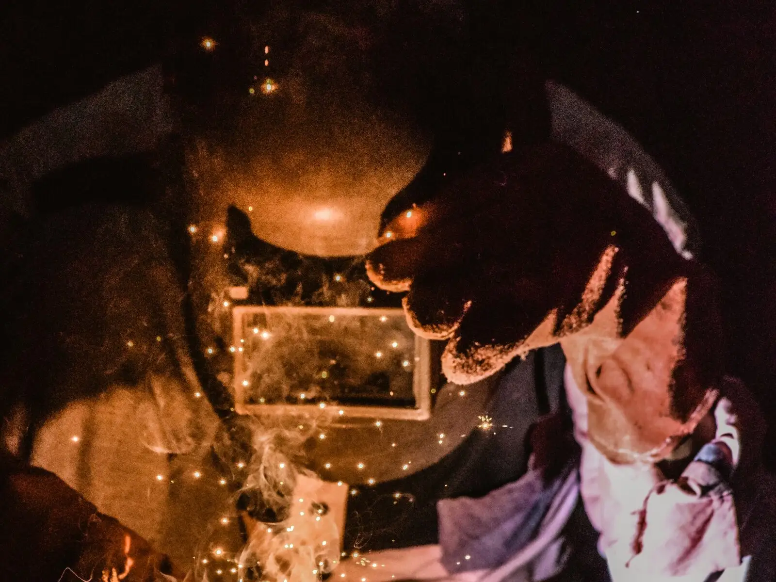 A fabricator in a welding mask welding steel at a workbench, sparks lighting his face shield.